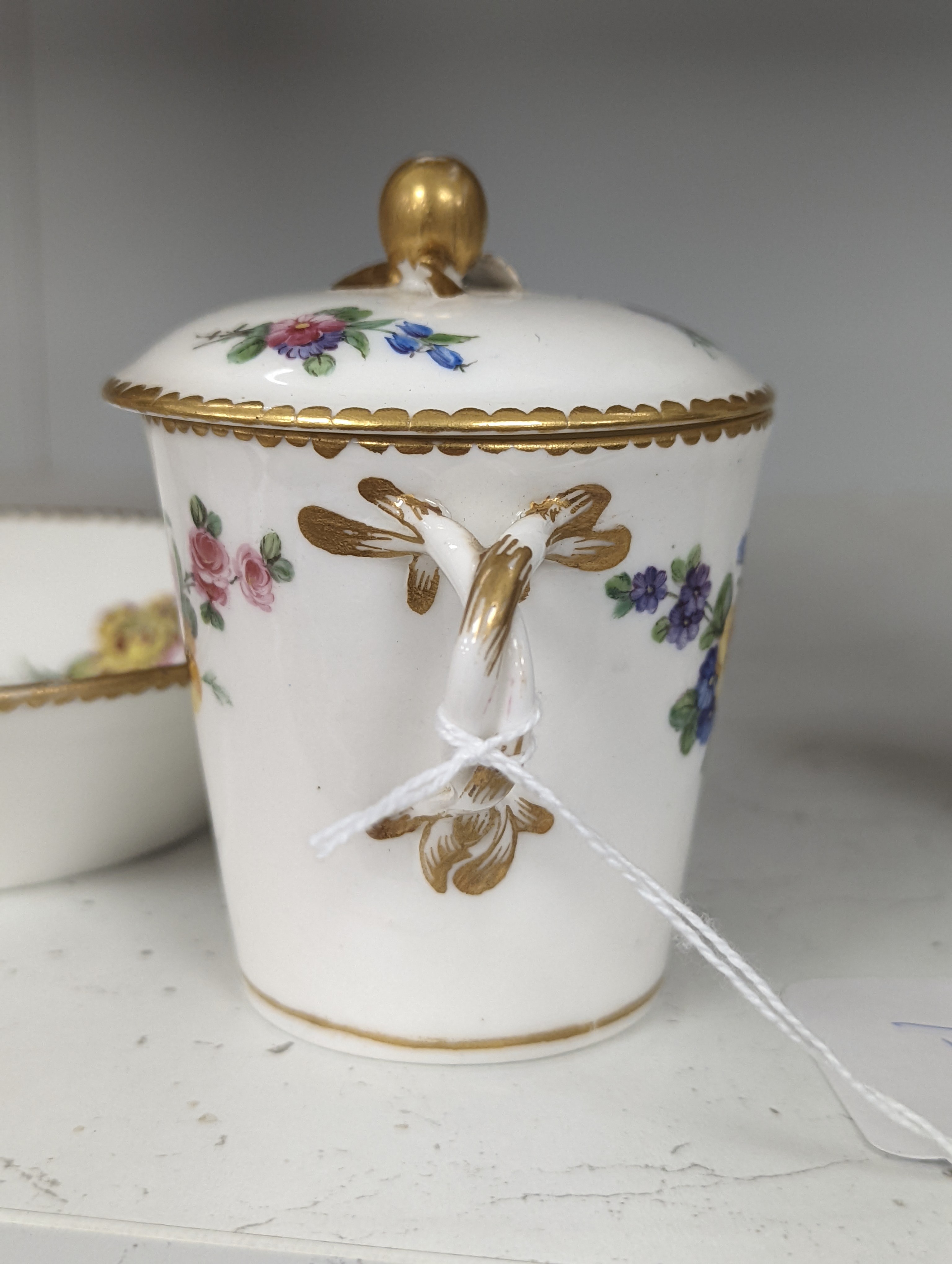 A Sevres tapering cup with entwined handle and cover and stand painted with flowers, date code for 1780, painters mark for Le Bel jnr., square incised marks, height 10.5cm